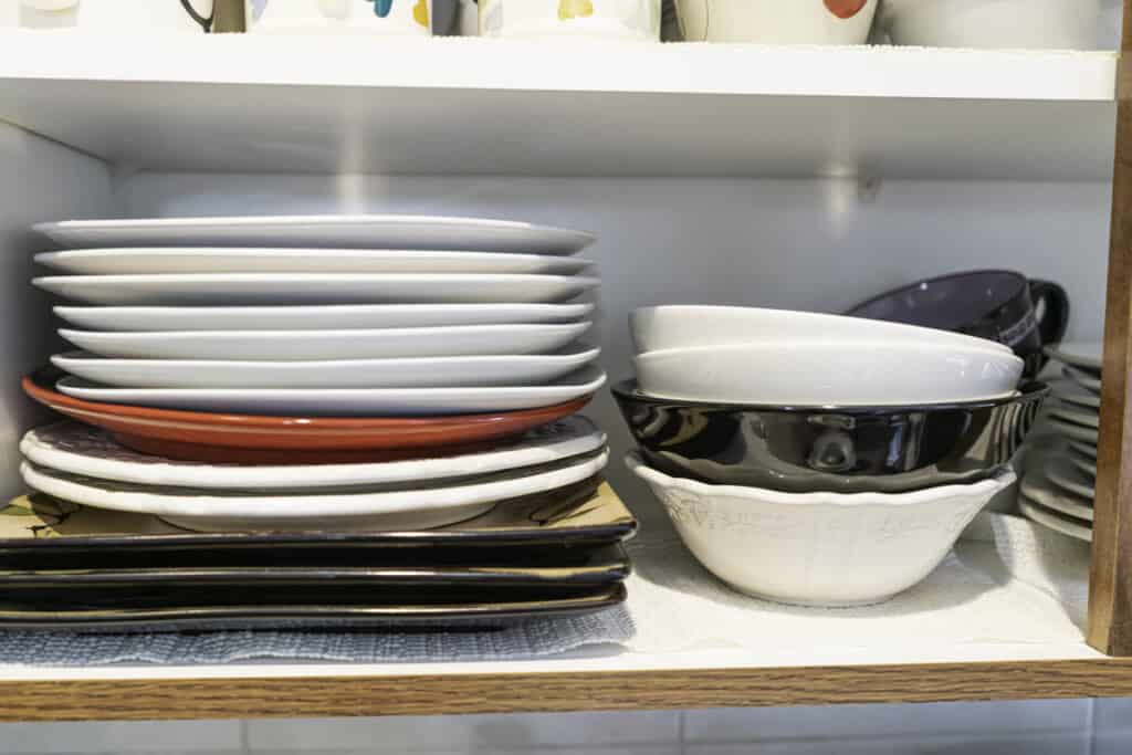 stack of non matching bowls and plates in kitchen cabinet