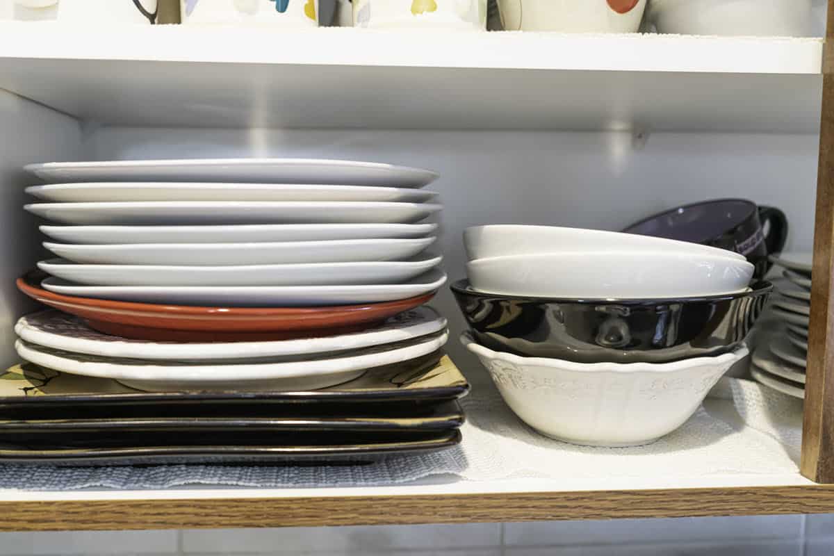 stack of non matching bowls and plates in kitchen cabinet